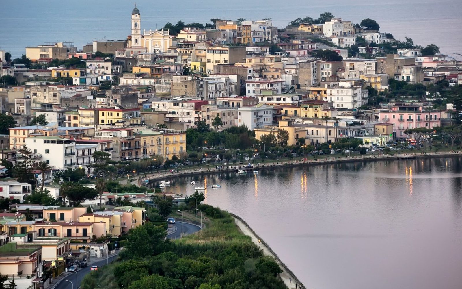 Il paese di Bacoli sul golfo al crepuscolo, con le luci che si riflettono sull'acqua immobile della costa flegrea