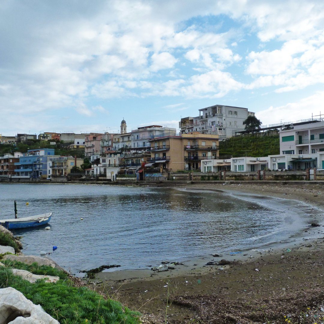 Le case pastello e la piccola spiaggia curva del borgo di pescatori di Bacoli con una barca blu ormeggiata in primo piano