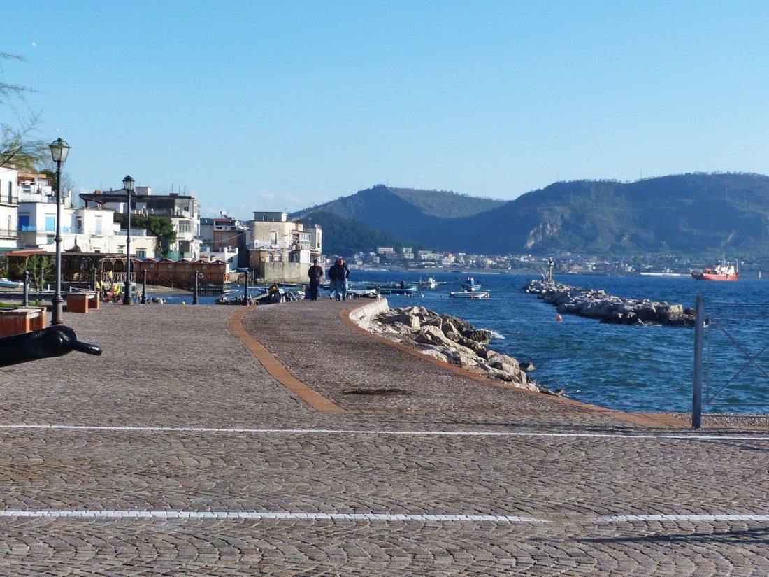 Il lungomare lastricato di Bacoli sul golfo di Pozzuoli, con barche da pesca e i promontori vulcanici sullo sfondo