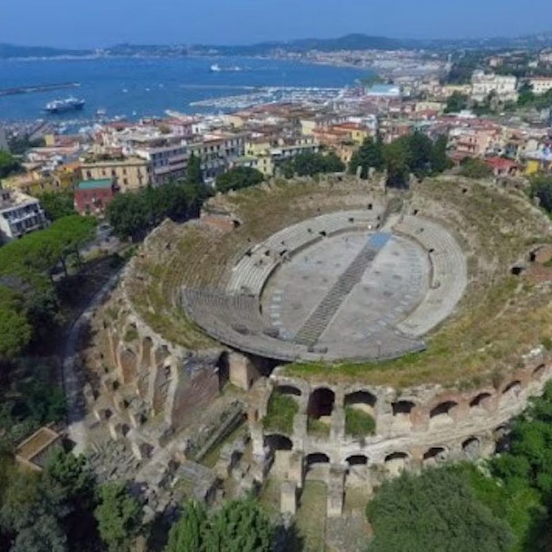 Veduta aerea dell'Anfiteatro Flavio ovale di Pozzuoli inserito nella città, con il golfo di Pozzuoli sullo sfondo