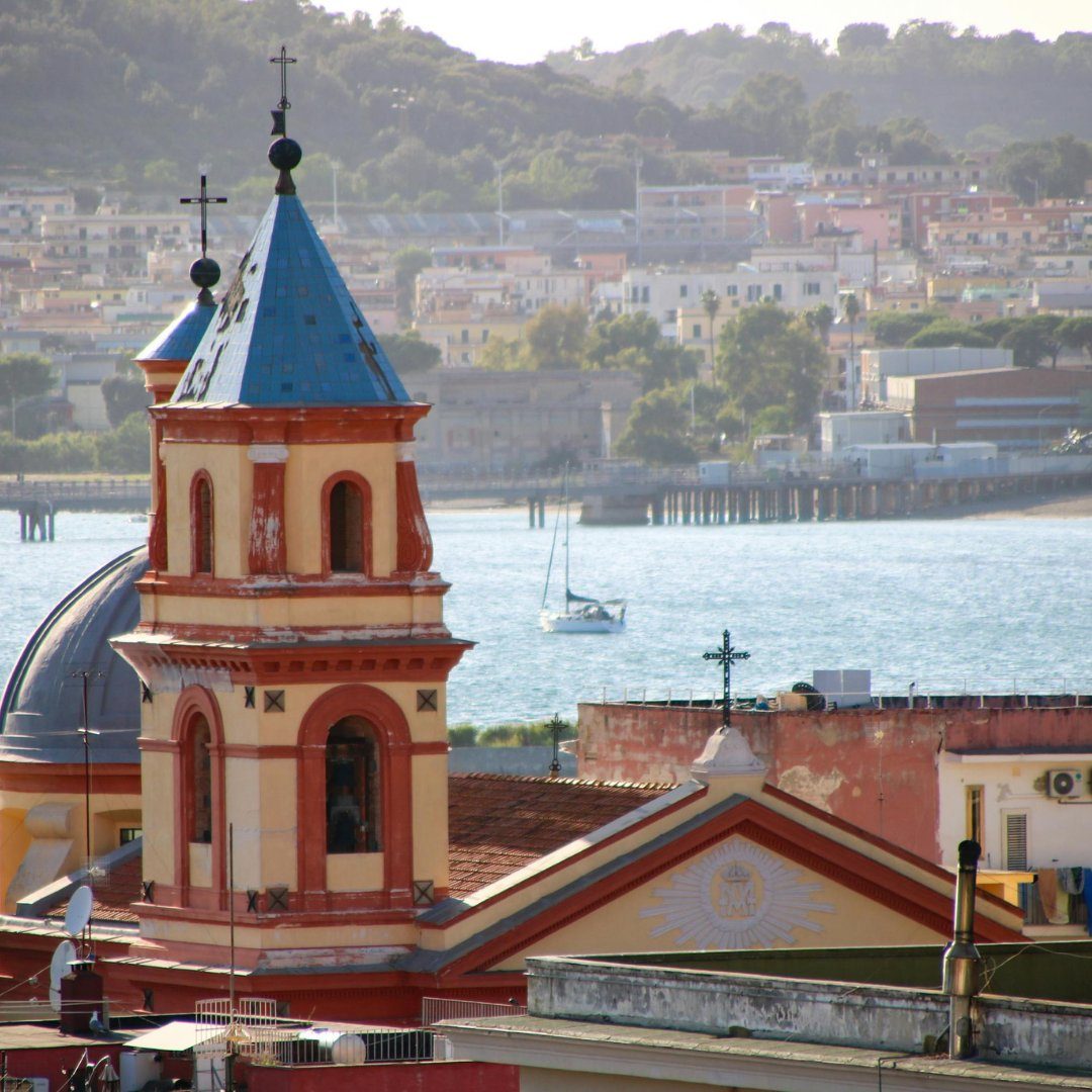 Un campanile barocco rosso e giallo con cupola in maiolica azzurra che si erge sopra i tetti e il porto di Pozzuoli