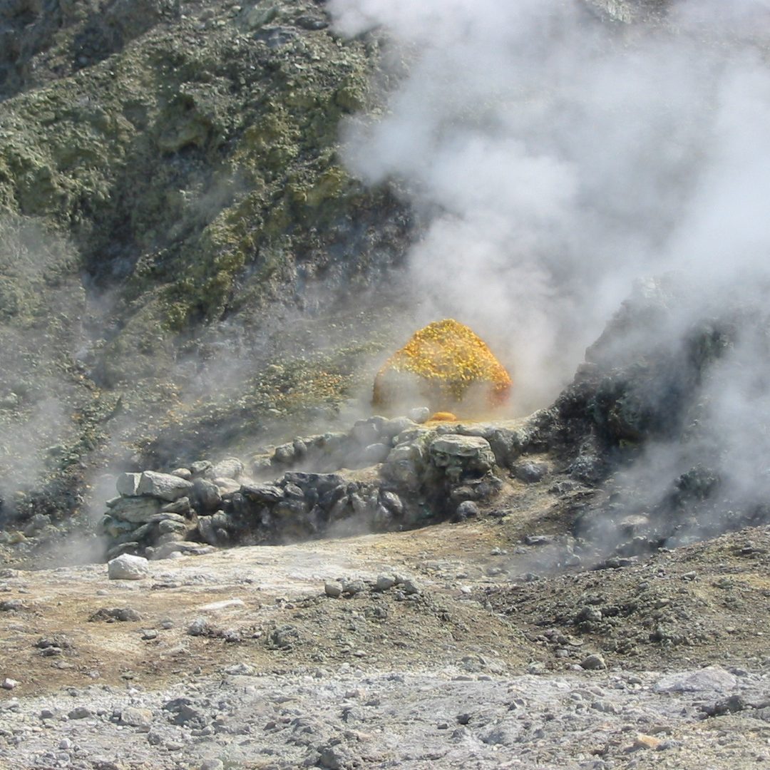 Primo piano di una fumarola della Solfatara — cristalli di zolfo giallo brillante attorno a una bocca che rilascia un denso vapore vulcanico bianco
