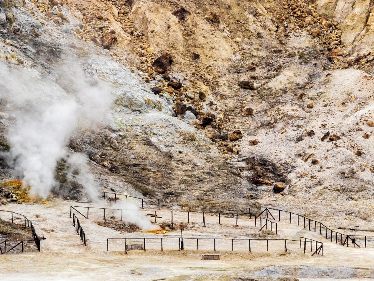 Il cratere della Solfatara a Pozzuoli — vapore bianco che si alza dalle fumarole su un fondo vulcanico pallido e striato di zolfo, cinto da ringhiere di sicurezza
